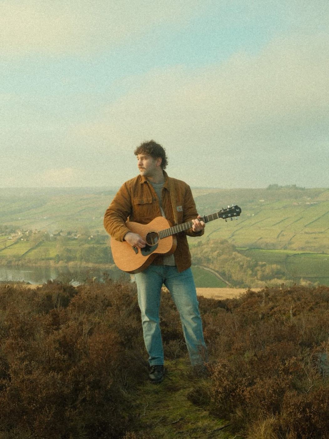 Connor Walsh playing acoustic guitar on a hillside