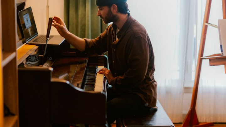 Musician at a piano with a laptop on a stand, managing the digital side of their music career